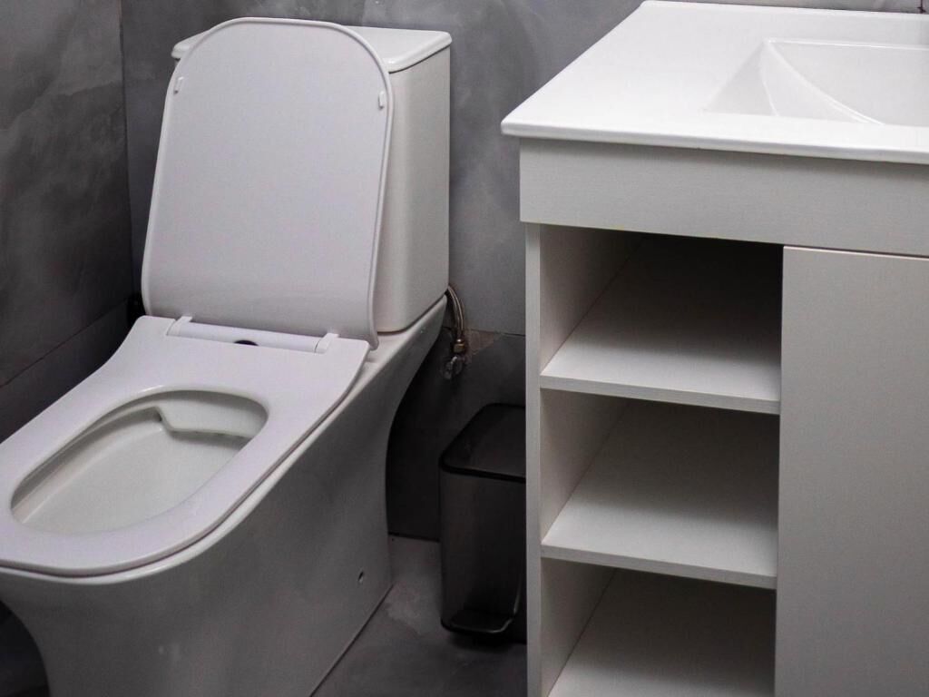 Un baño moderno con inodoro, un bote de basura y un estante blanco.