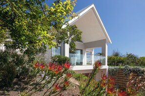 Een modern huis met balkon, omringd door weelderige begroeiing en bloeiende planten.