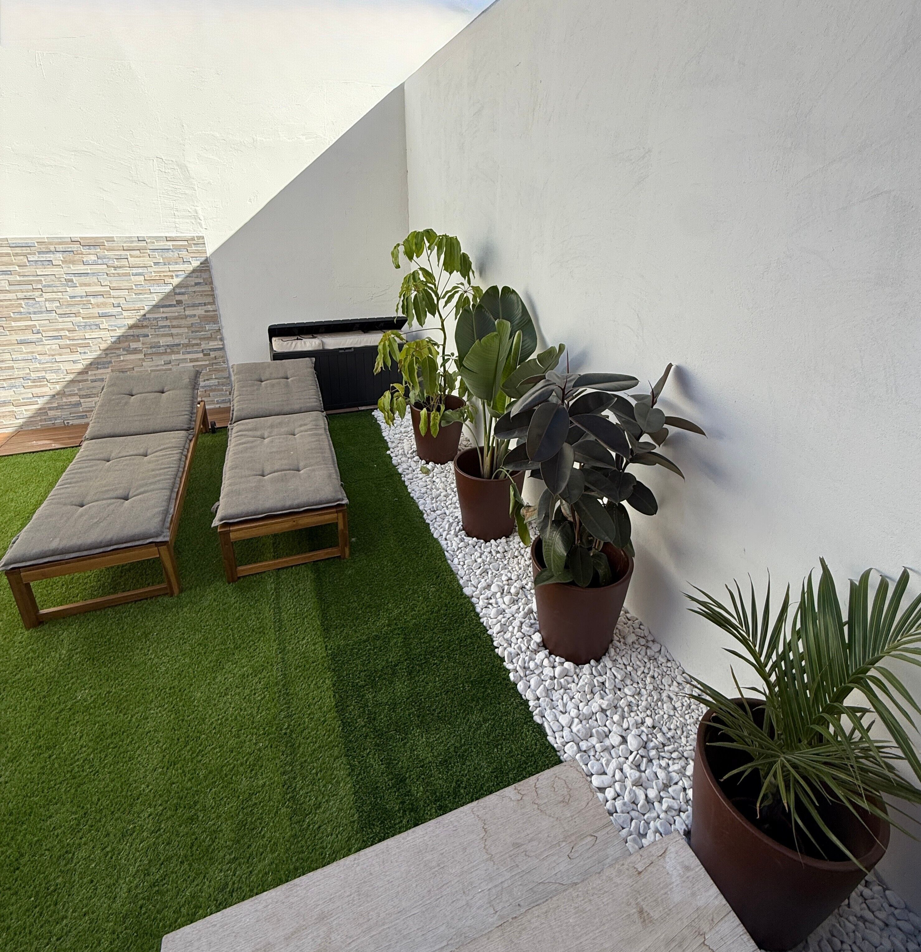 Una terraza en la azotea con césped artificial, un espacio de descanso con cojines y plantas en macetas.