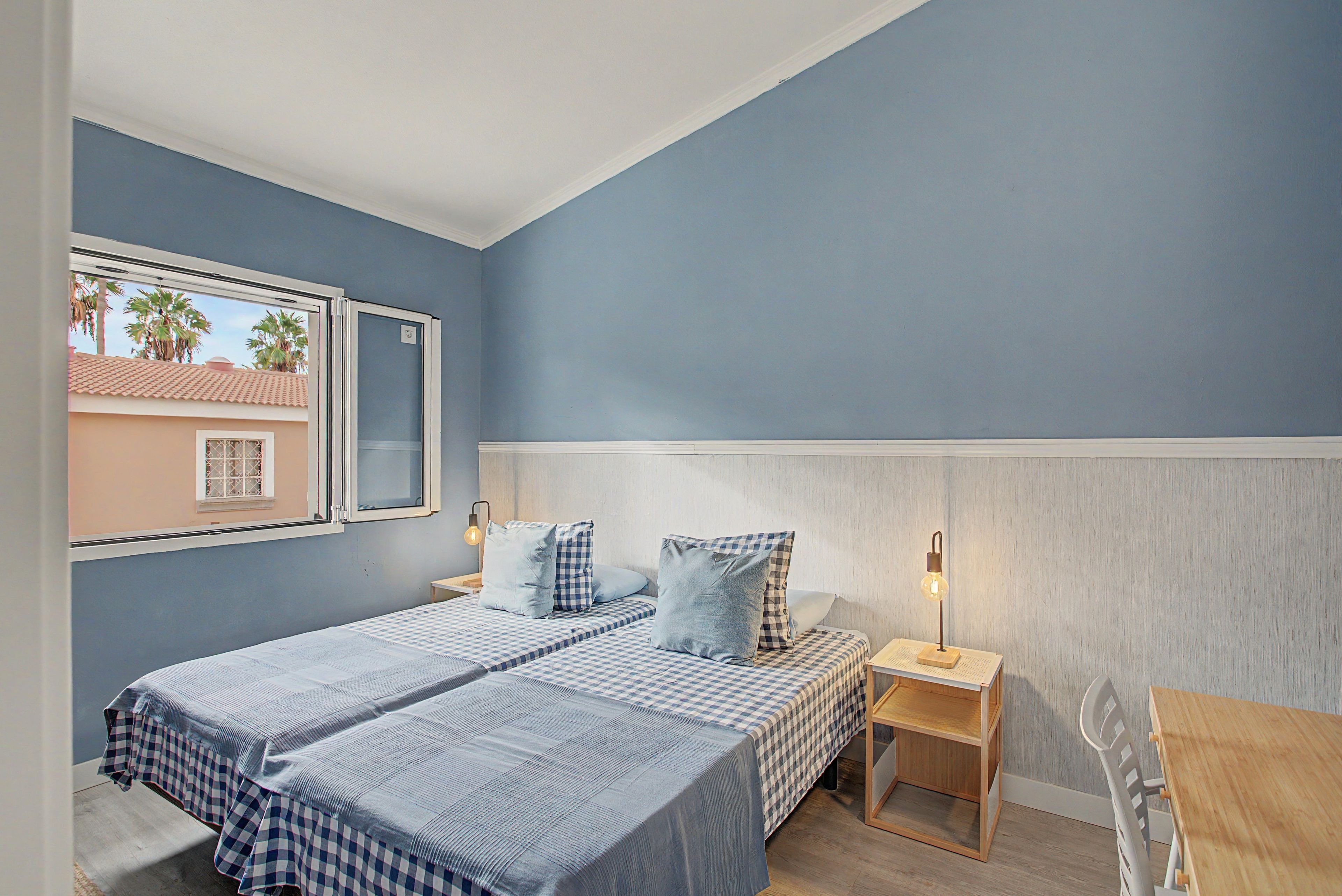 A bedroom with a bed, two bedside tables, a nightstand, and a window.