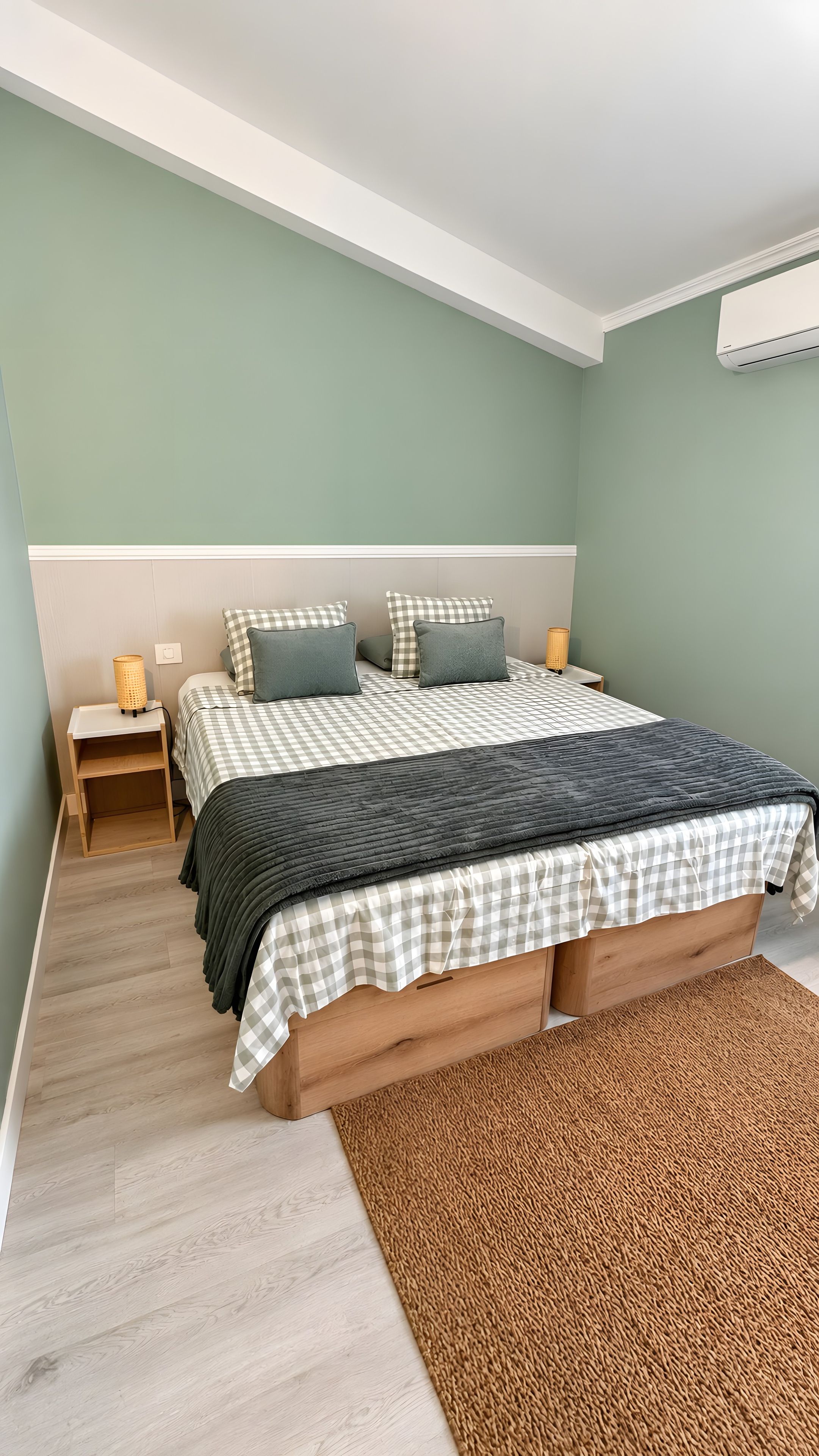 A bedroom with a bed, nightstands, a lamp, and a wall-mounted air conditioner.