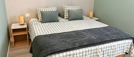 A bedroom with a bed, nightstands, a lamp, and a wall-mounted air conditioner.