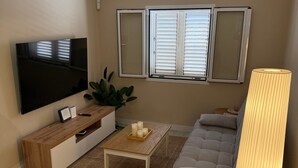 En stue med et fladskærms-tv, et træbord, en sofa og en lampe.