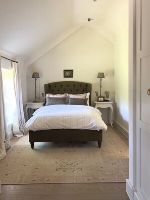 Un dormitorio con una cama grande, dos mesitas de noche, una ventana con cortinas e imagen en la pared.