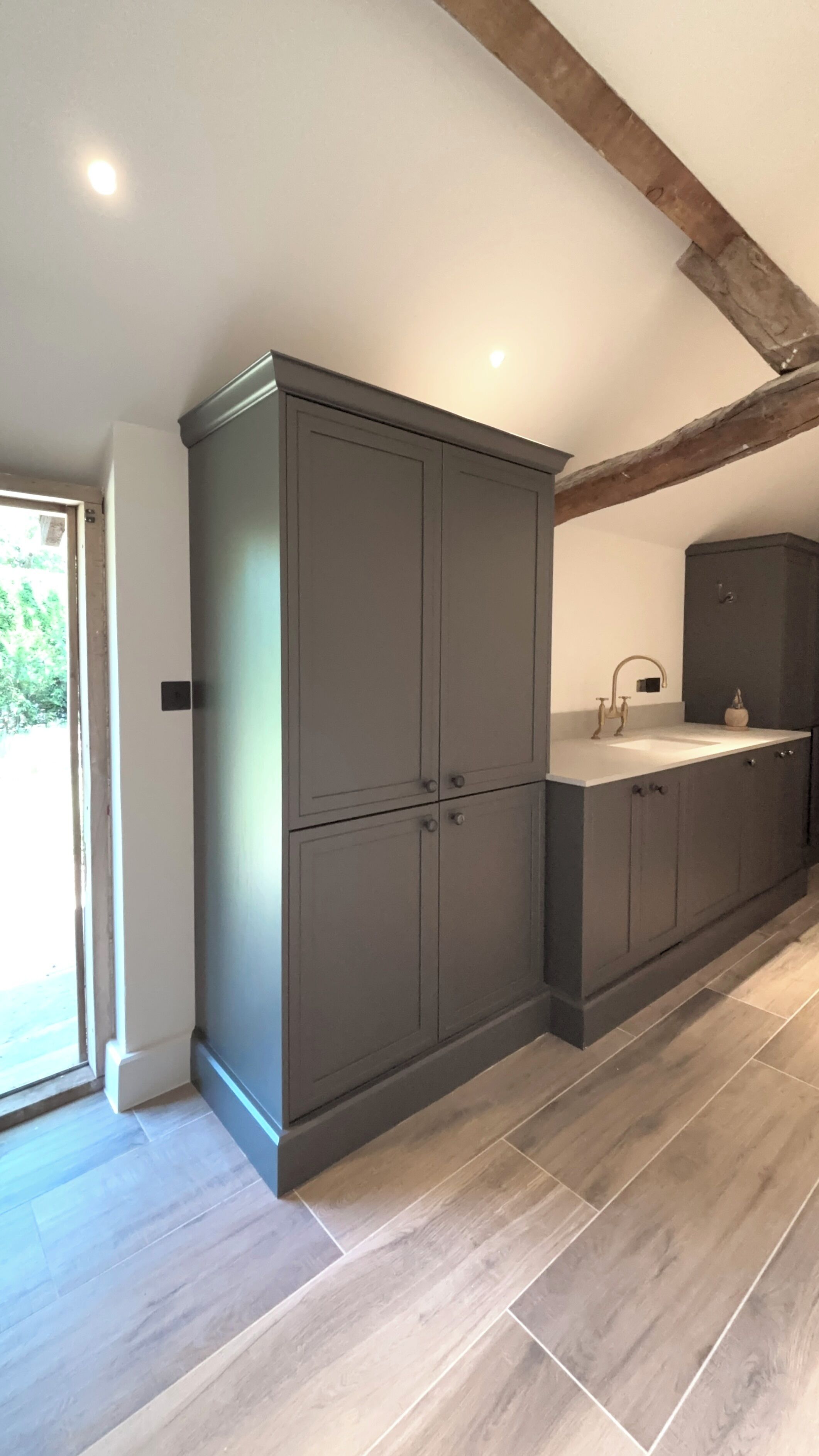A kitchen with grey cabinets, a white countertop, and a wooden floor.