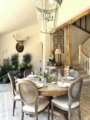 A dining area with a round table set for six, surrounded by wicker chairs. A mounted moose head decorates the wall above the table.