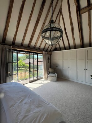 A bedroom with a large bed, a chair, a wardrobe, and a view through a glass door.