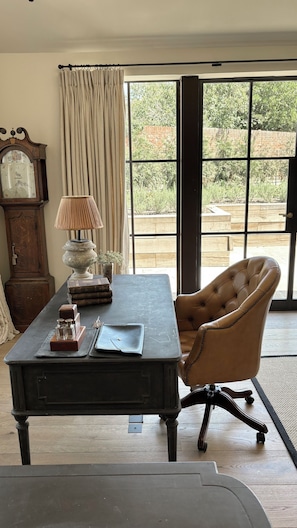 Una habitación con escritorio, silla, lámpara, reloj y vistas a zonas verdes.