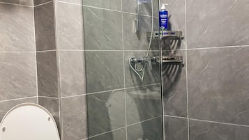 Un baño con ducha envuelta en vidrio, inodoro y perchero para toallas.