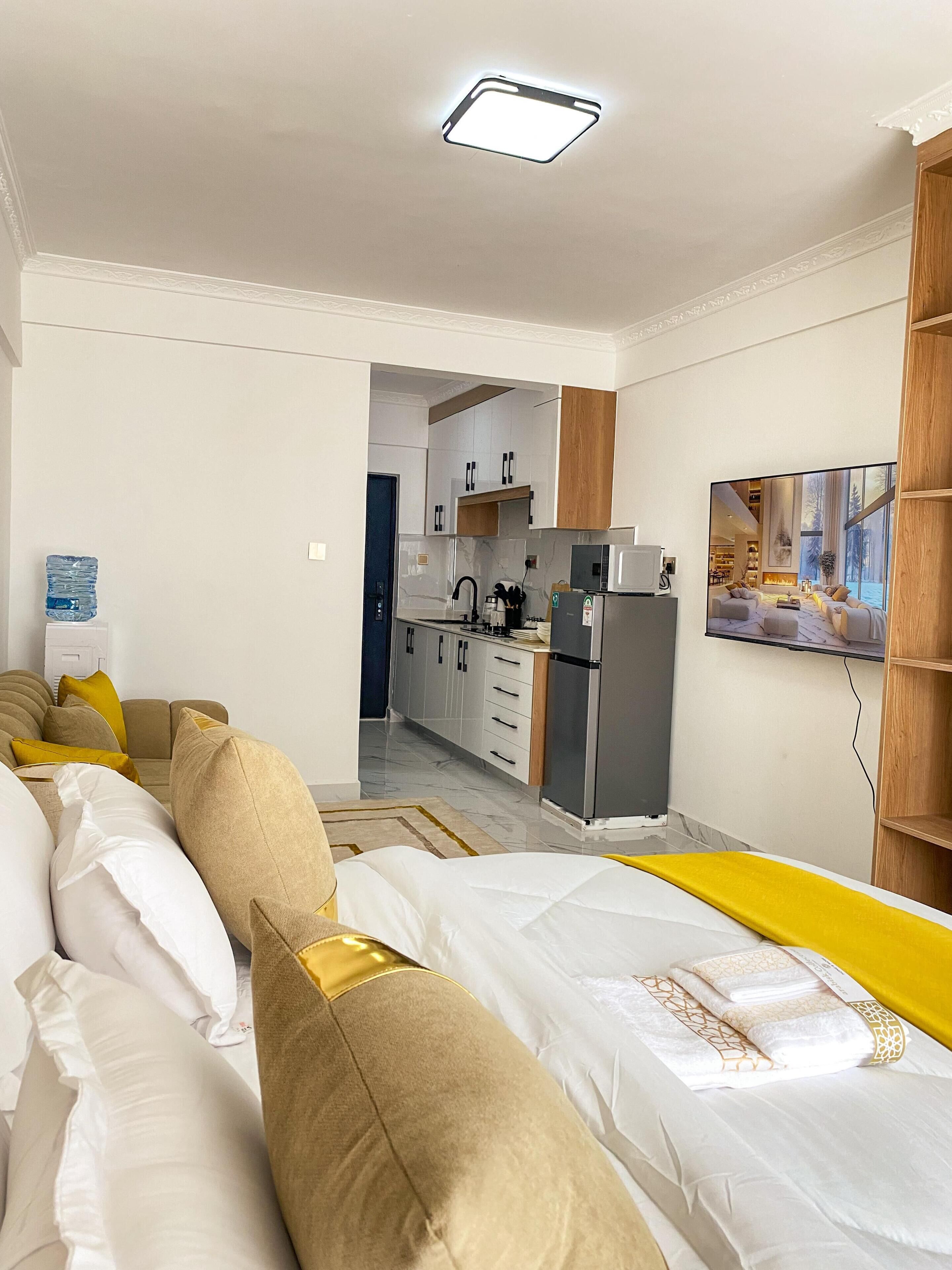 Una sala moderna con sofá, cama, cocina al fondo y un ventanal grande.