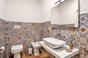 Een badkamer met toilet, bidet en een groot wit wastafelmeubel met spiegel.