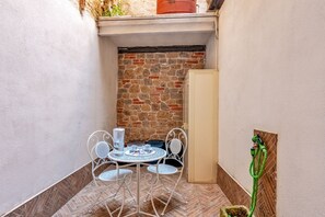 A small outdoor patio with a round table and chairs, a potted plant, and a wall with a stone pattern. - GuestHost - Iglesias Modern Apartment (sleeps 4) (Iglesias)