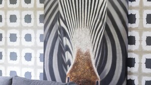 Une peinture représentant un zèbre sur un mur recouvert d’un papier peint à motifs géométriques.