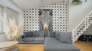 Un salon moderne avec un canapé d’angle gris, une table basse ronde et un escalier doté d’une rampe blanche.