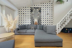 Ein modernes Wohnzimmer mit einem grauen Ecksofa, einem runden Couchtisch und einer Treppe mit weißer Geländer.