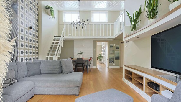 Un salon moderne avec un canapé d’angle, un téléviseur à écran plat et un coin repas donnant sur un escalier menant à l’étage supérieur.