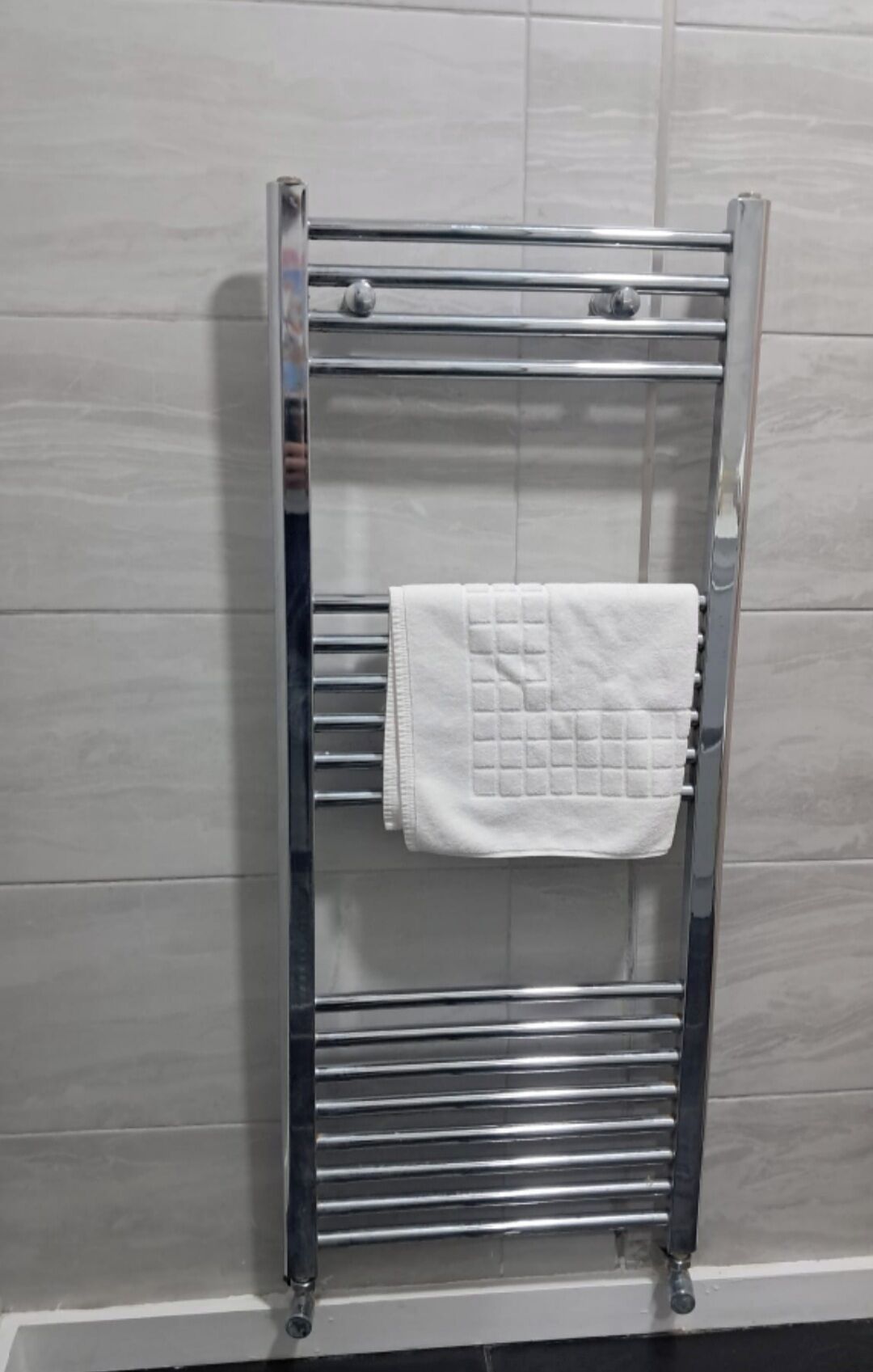 Ein Metallhandtuchhalter mit zwei horizontalen Stangen und einem gefalteten Handtuch.