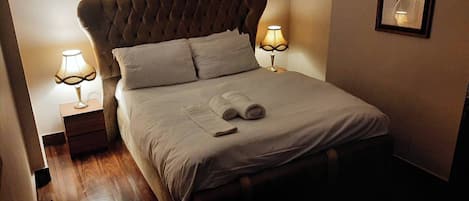 A neatly made bed with pillows and a rolled towel, two bedside lamps, and a framed picture on the wall.