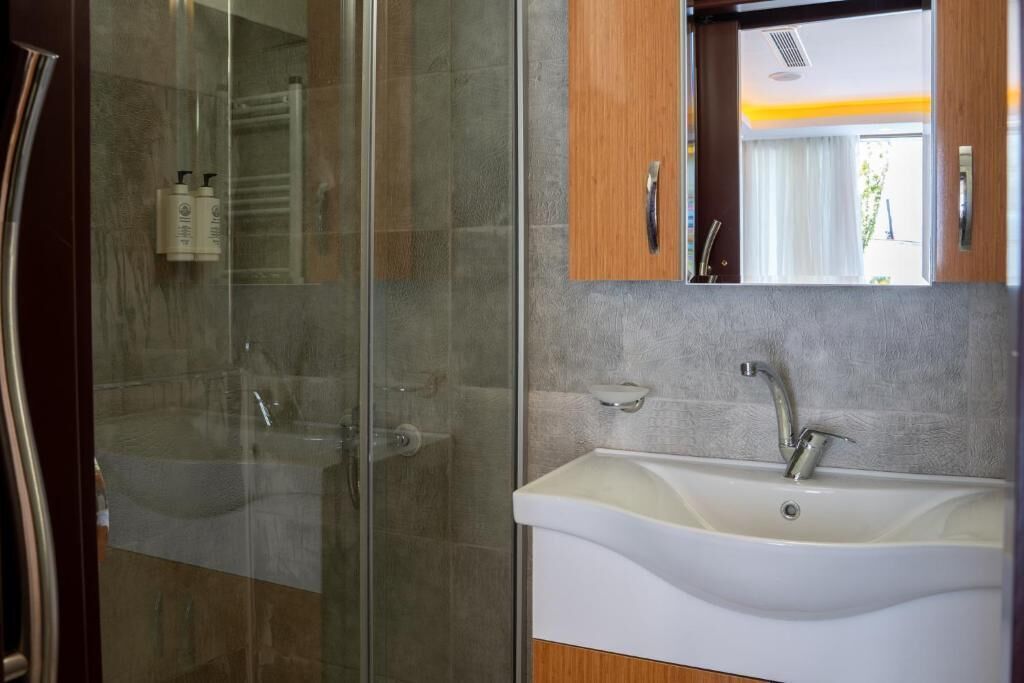Een moderne badkamer met een douchecabine van glas, een witte wastafel met één kraan en houten kasten.