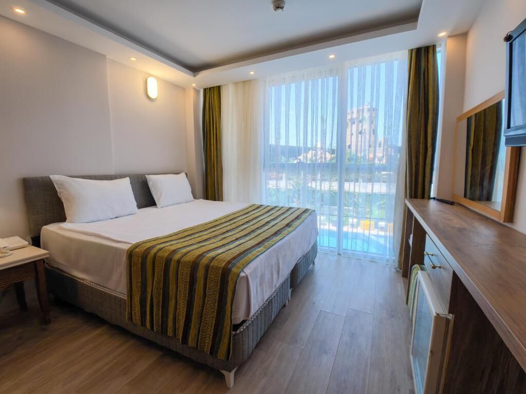 A hotel room with a large bed, a desk, a mirror, and a view of the city.