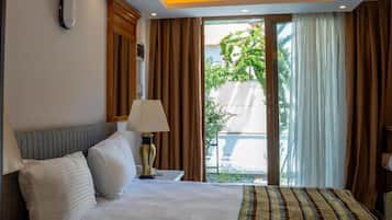 Habitación de hotel con cama, mesita de noche, lámpara y vista al exterior por una puerta corredera.