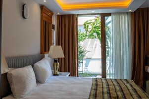 Habitación de hotel con cama, mesita de noche, lámpara y vista al exterior por una puerta corredera.