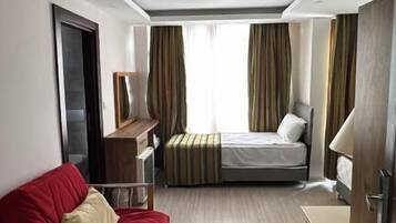 Une chambre d’hôtel de taille modeste, comprenant un lit, un canapé rouge, une petite table et une armoire.