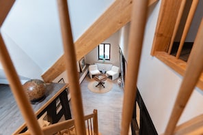 Een loft-stijl kamer met een hoge plafond, houten balken, een ronde houten tafel, twee witte stoelen en een wereldbol op een tafel.