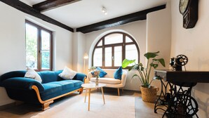 Una sala de estar con un sofá azul, un sillón blanco, una mesita y una máquina de coser.