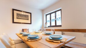 Un comedor con una mesa de madera dispuesta para cuatro, un cuadro en la pared y una ventana con vistas al exterior.