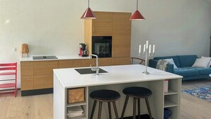 Moderni keittiö, jossa on keskeinen saareke, puukaapit ja punainen riippuvalaisin.