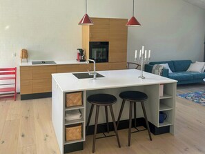 A modern kitchen with a central island, wooden cabinets, and a red pendant light. - Undisturbed house at the foot of Mols Bjerge (Knebel)