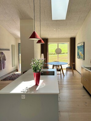 A modern kitchen with a central island, pendant lights, and a view of the outdoors. - Undisturbed house at the foot of Mols Bjerge (Knebel)