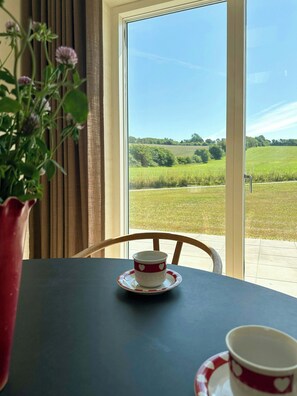 A table with a cup and saucer, a chair, a window with a view of a green field, and a potted plant. - Undisturbed house at the foot of Mols Bjerge (Knebel)