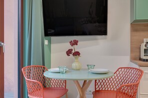 Ein Essbereich mit einem runden Tisch, zwei Stühlen, einer Blumenvase und einem an der Wand befestigten Flachbildfernseher.