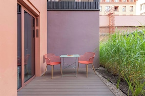 Eine Terrasse im Freien mit zwei roten Stühlen und einem Tisch, einer Glast ür und einer Metalltreppe.