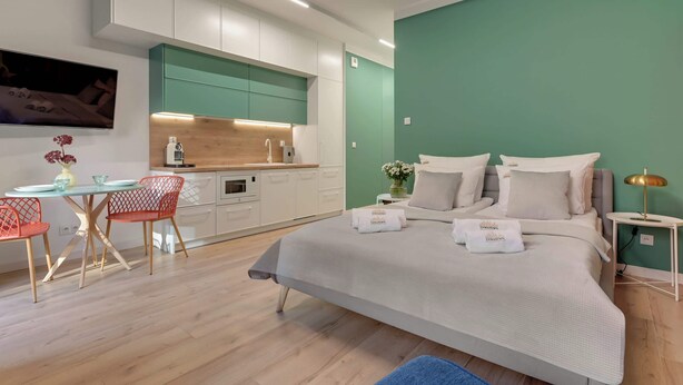 A modern bedroom with a bed, a small table with chairs, a TV, and a kitchenette. - Granaria A105 | Terrace | Perfect for Couples (Gdańsk)