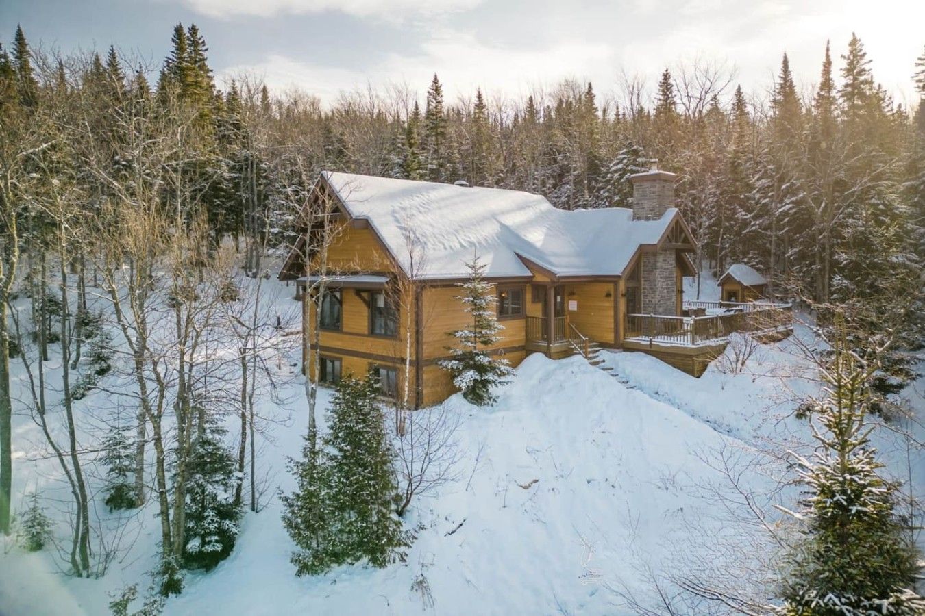 A log cabin with a stone chimney, surrounded by a snowy forest.