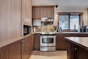 A kitchen with wooden cabinets, a stainless steel stove, and a window with a view of trees. - The Little Alpine - Spa & Mountain (Petite-Rivière-Saint-François)