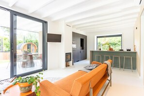 A modern living space with a sofa, a dining area, a kitchen, and a sliding glass door leading to an outdoor area.