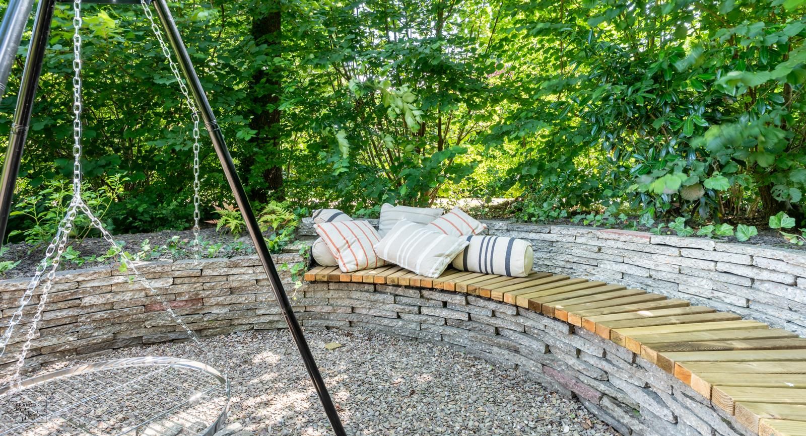 A curved wooden bench with cushions in a garden setting.