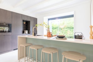 A modern kitchen with a bar area, built-in appliances, and a large window offering a view of greenery.