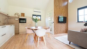 Een moderne keuken met een eethoek, houten vloer en een flatscreen televisie bevestigd aan een houten paneelwand.