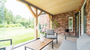 Een overdekt terras met een houten plafond, bakstenen muren en uitzicht op een gazon.