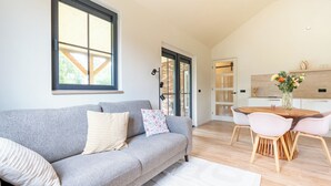 Een moderne woonkamer met een grijze bank, een eettafel met stoelen, en een keuken op de achtergrond.