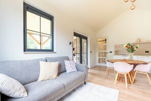 A modern living room with a grey sofa, a dining table with chairs, and a kitchen area in the background. - Detached, single-storey holiday home with hot tub, spacious terrace and bike shed, surrounded by Drenthe nature. (Gasselte)