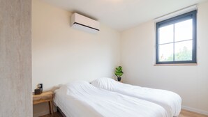 Een slaapkamer met twee bedden, een raam, een airconditioning en een kleine plant.