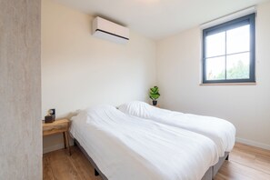 A bedroom with two beds, a window, an air conditioning unit, and a small plant. - Detached, single-storey holiday home with hot tub, spacious terrace and bike shed, surrounded by Drenthe nature. (Gasselte)