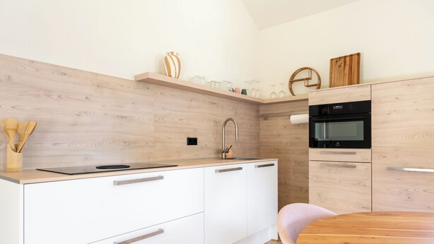 Een moderne keuken met witte kastjes, een inbouwoven en een houten eettafel.