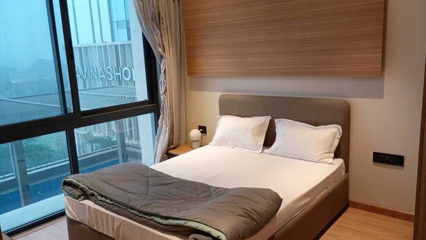 A modern hotel room with a large window, a bed with white linens, and a view of the cityscape.